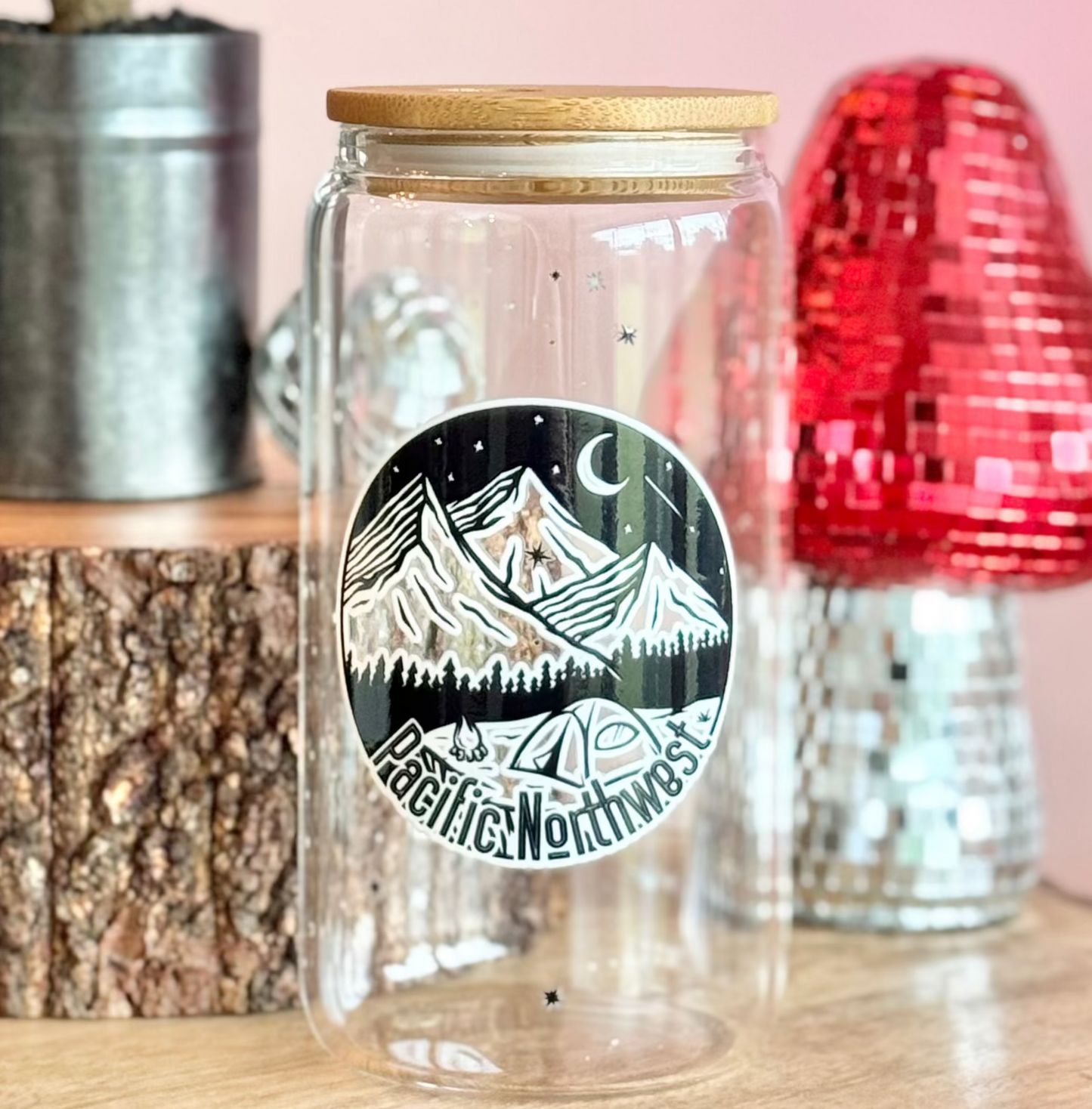 Clear glass jar with mountain design on a wooden surface with decorative items.