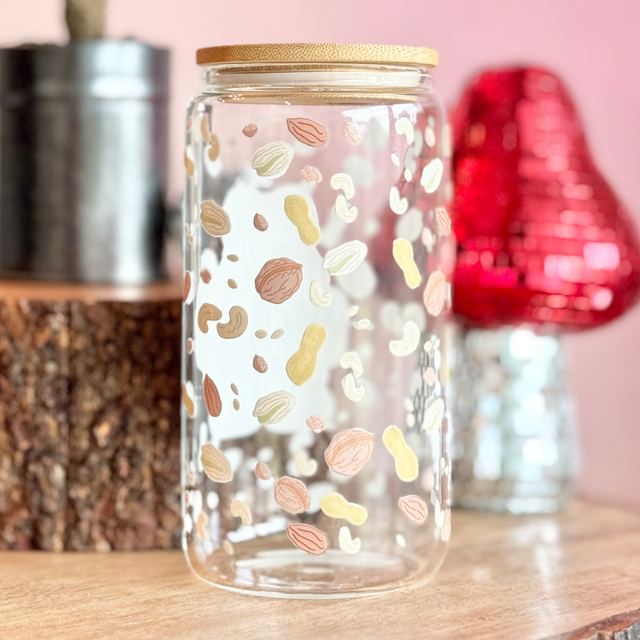 Decorative glass jar with colorful patterns on a wooden surface with a pink background.