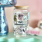 Glass jar with decorative text and illustrations on a light blue stand with a pink background