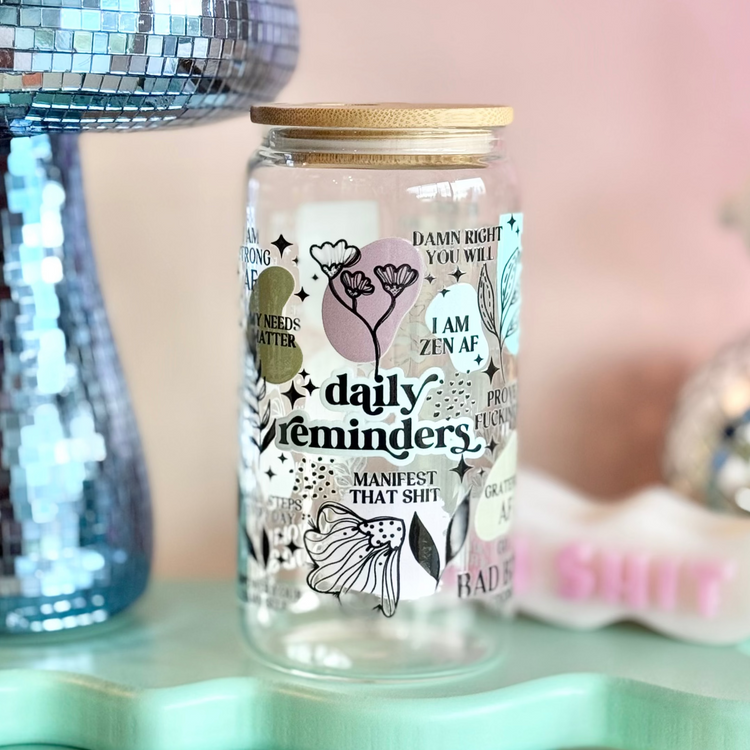 Glass jar with decorative text and illustrations on a light blue stand with a pink background