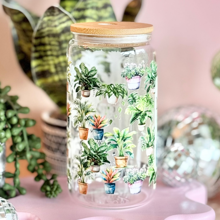 Decorative glass jar with plants on a pink stand, surrounded by festive decorations.