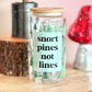 Glass jar with 'snort pines not lines' text on a wooden surface with decorative items.