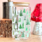 Glass jar with tree pattern on a wooden surface with decorative items in the background