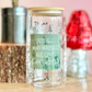 Clear glass jar with a green label on a wooden surface with decorative items in the background.