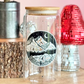 Clear glass jar with mountain design on a wooden surface with decorative items.