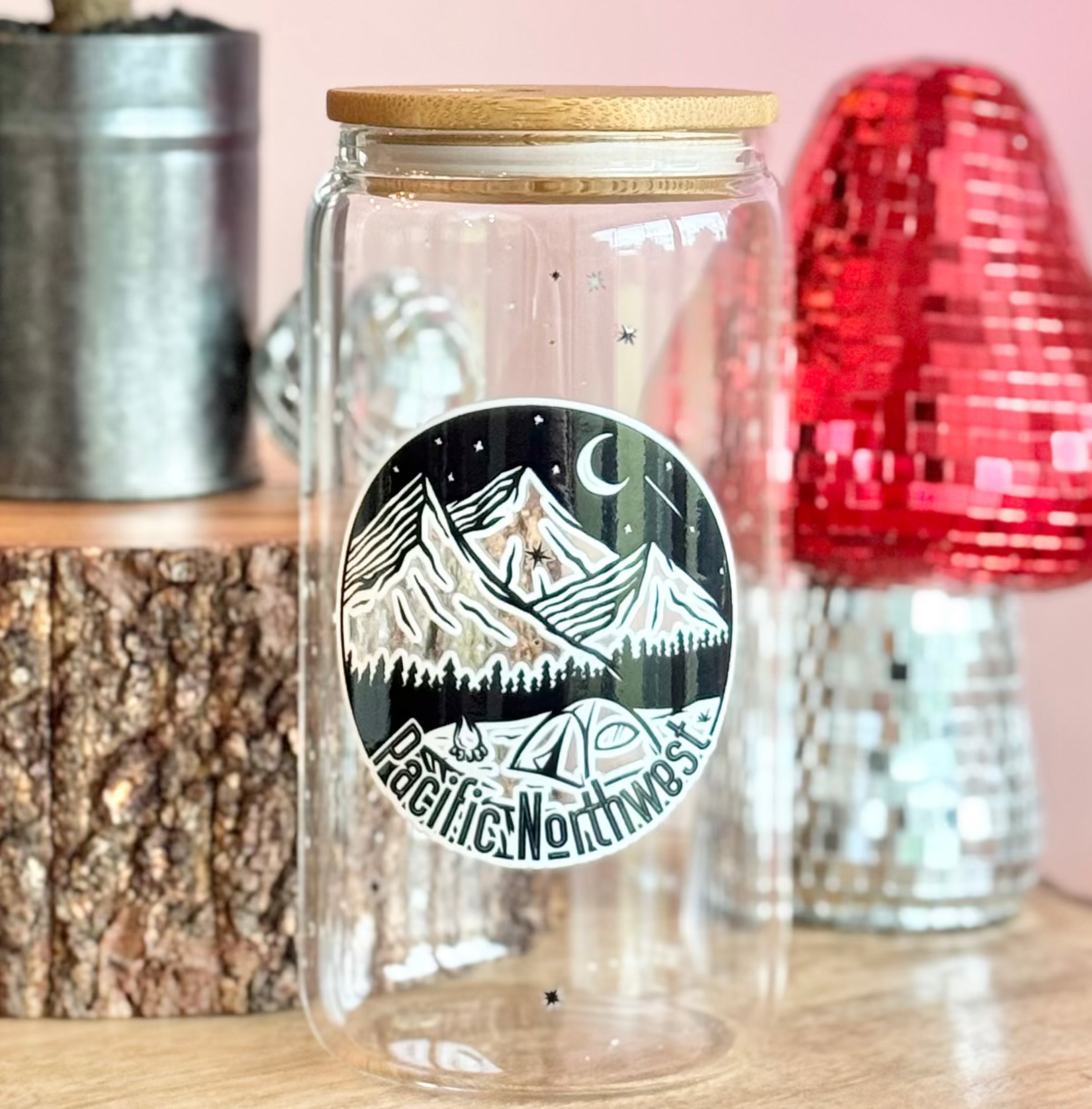 Clear glass jar with mountain design on a wooden surface with decorative items.