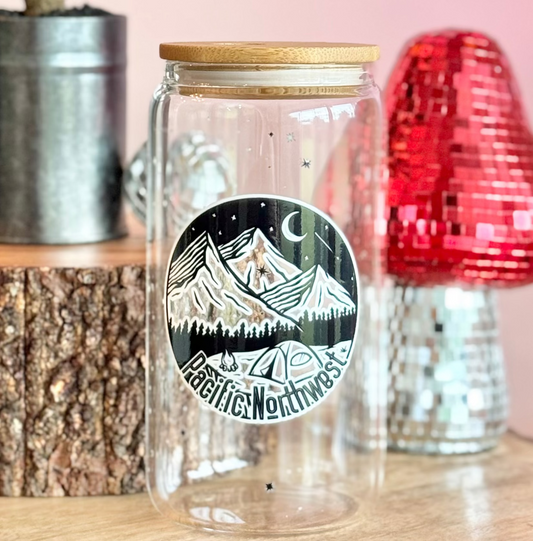 Clear glass jar with mountain design on a wooden surface with decorative items.