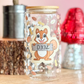 Decorative glass jar with a squirrel design on a wooden surface with a pink background.