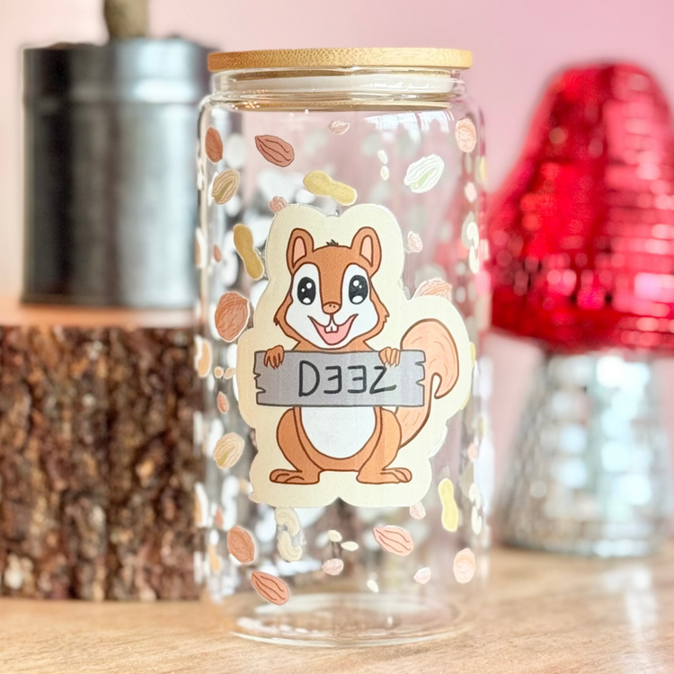 Decorative glass jar with a squirrel design on a wooden surface with a pink background.