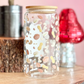 Decorative glass jar with colorful patterns on a wooden surface with a pink background.