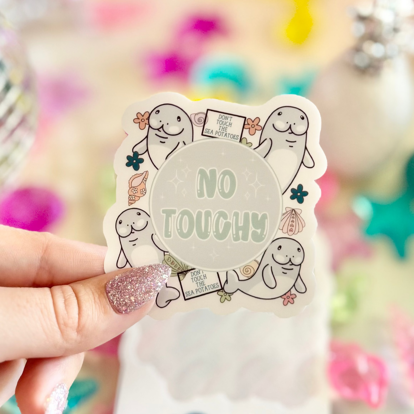 Hand holding a sticker with 'No Touchy' text amidst colorful decorative items