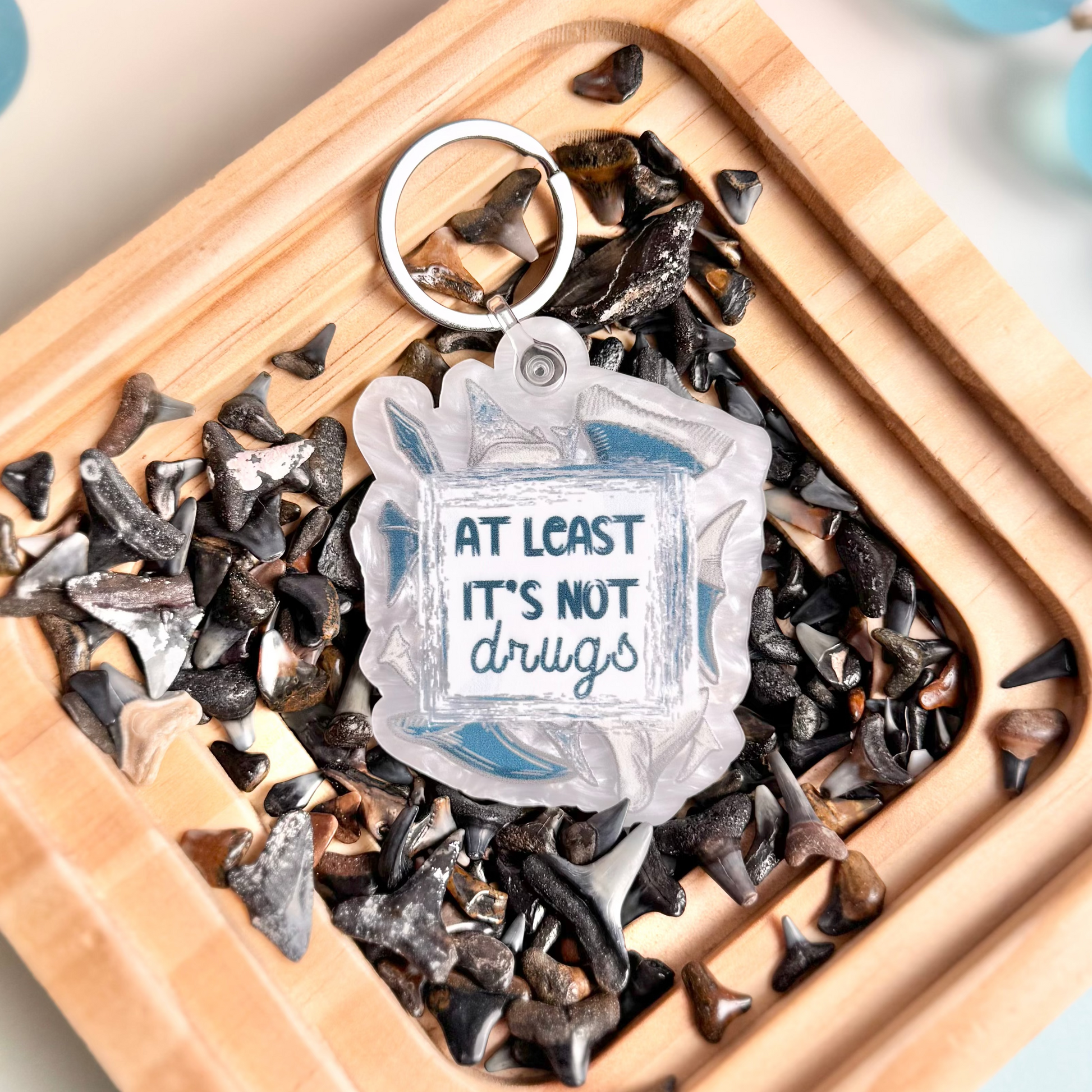 Keychain with 'At least it's not drugs' text on a wooden tray with decorative elements.